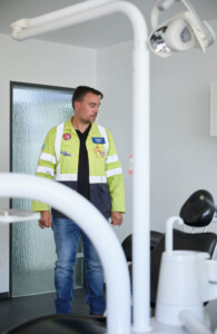 Ein Mann in gelber Arbeitsjacke steht in einer Zahnarztpraxis.