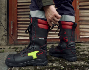 Eine Person in schwarzen Feuerwehrstiefel, mit roten und gelben Akzenten. Auf den Schuhe sind Gefahrensymbole und die Aufschrift ELTEN zu sehen.