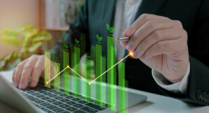 Ein Mann in Anzug arbeitet an einem Laptop, während er mit einem Stift eine virtuelle, grüne Wachstumsstatistik verfolgt. Die Grafik zeigt aufsteigende Balken mit kleinen Blättern an der Spitze, die Nachhaltigkeit und wirtschaftliches Wachstum symbolisieren. Im Hintergrund sind Pflanzen und ein Büroambiente zu erkennen.