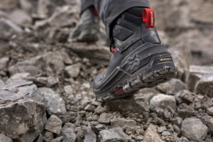 Ein schwarzer Sicherheitsschuh mit robuster Profilsohle auf felsigem Untergrund. Die Sohle zeigt eine Michelin-Logo-Prägung, und der Schuh verfügt über rote Details sowie eine „Würth MODYF“-Schlaufe an der Ferse.