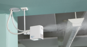 Nahaufnahme eines an der Decke montierten Luftbefeuchters, der feinen Nebel in einen Raum versprüht. Das Gerät ist mit Kabeln verbunden und befindet sich in einem modern gestalteten Innenraum mit einer Deckenbeleuchtung im Hintergrund.