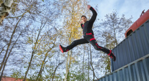 Ein Mann in schwarz-roter Arbeitskleidung springt von einem Container.