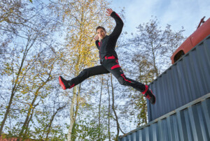 Ein Mann in schwarz-roter Arbeitskleidung springt von einem Container.