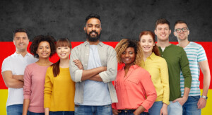 Gruppe junger Menschen unterschiedlicher Herkunft lächelt vor einer Deutschlandflagge.