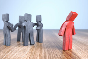 Eine Darstellung von fünf stilisierten Figuren, wobei vier davon miteinander interagieren und eine davon abseits steht und isoliert wirkt. Die isolierte Figur ist rot, während die anderen schwarz sind.