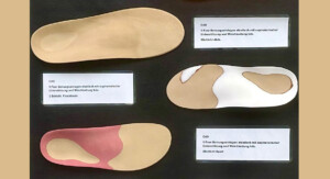 Nahaufnahme einer Präsentationswand mit mehreren orthopädischen Einlagen in unterschiedlichen Formen und Farben; kleine Beschriftungsschilder erklären die Modelle.